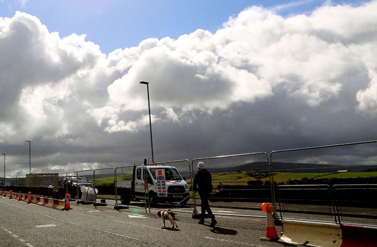 Pedestrain walking his dog on the road, behind safety barriers.
Large, fluffy clouds in the background