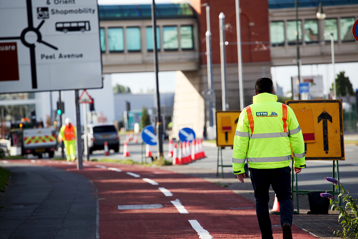 Go Traffic Management employee walking a cycle lane, towards safety signage and site. He is wearing a high vis jacket with the GTM logo