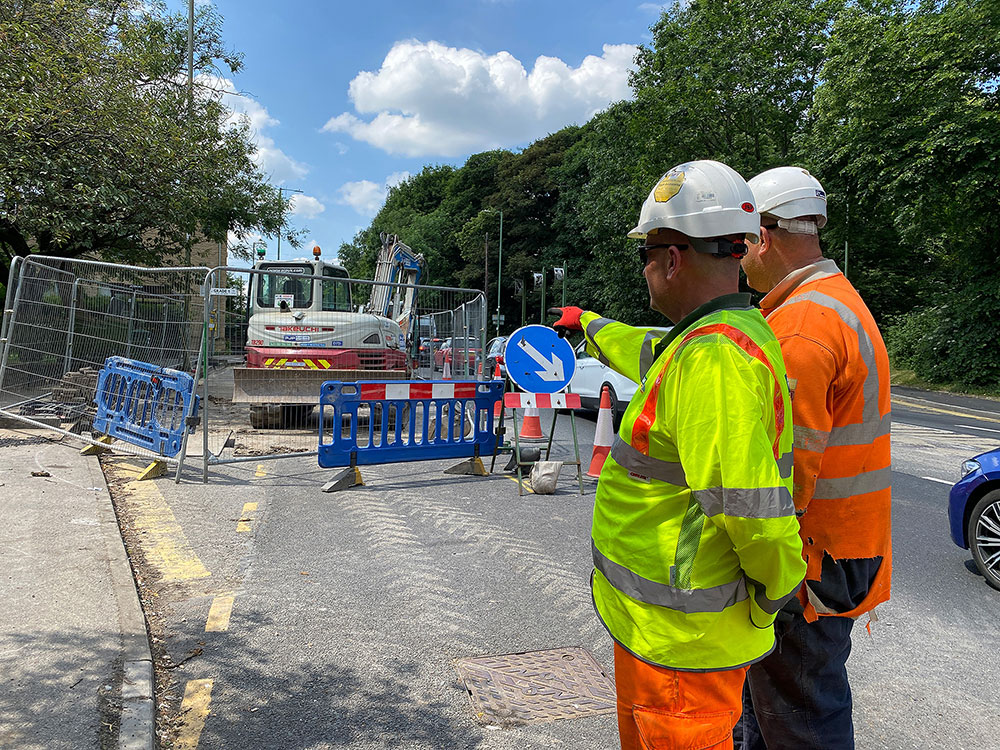 Colleague with client on site, both wearing full PPE. Colleague is pointing to the site, where you can see safety barriers and signs, as well as a large machine.